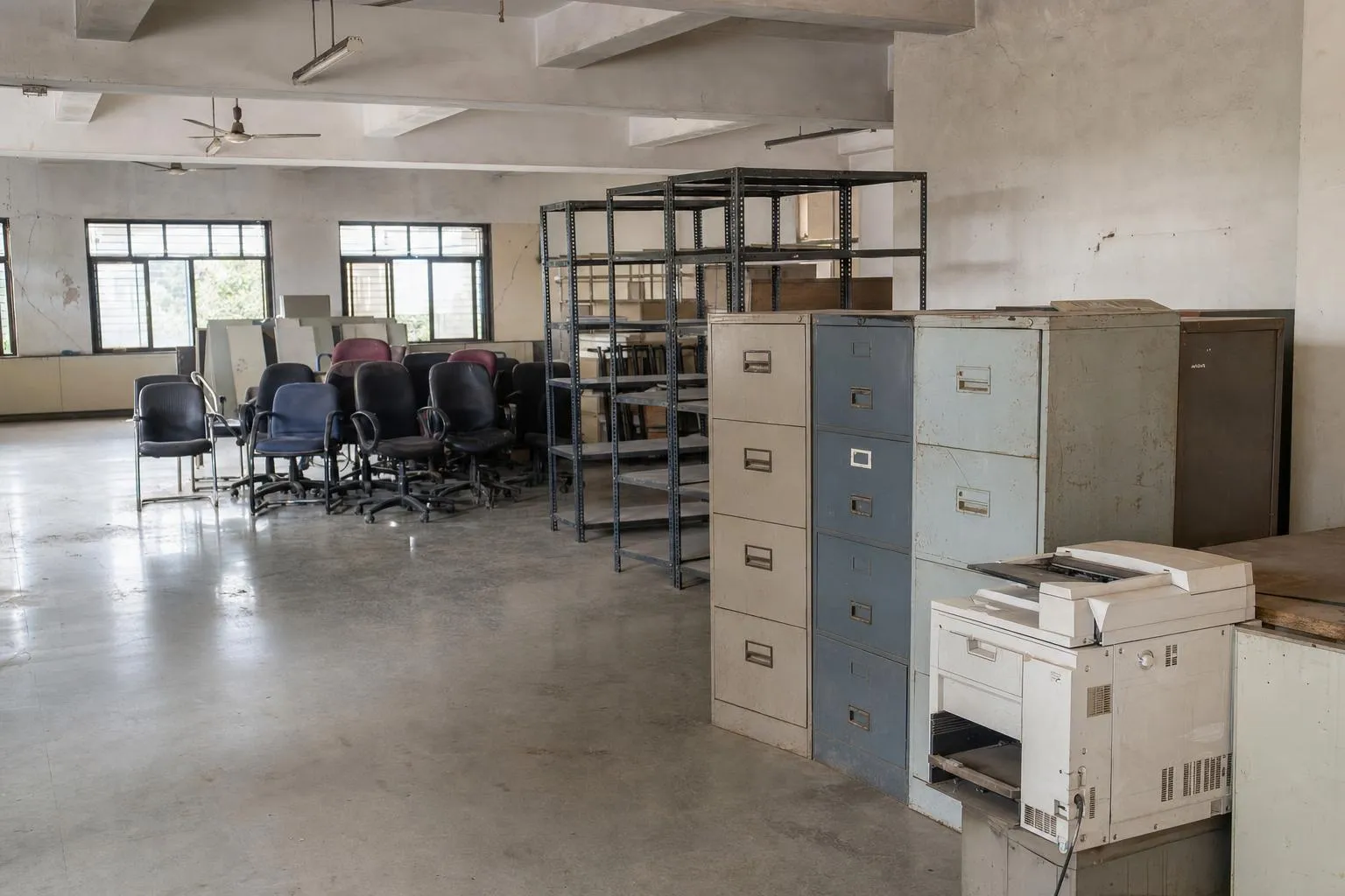 A cleared office floor with redundant equipment stacked ready for removal: metal filing cabinets, shelving frames, office chairs and a photocopier